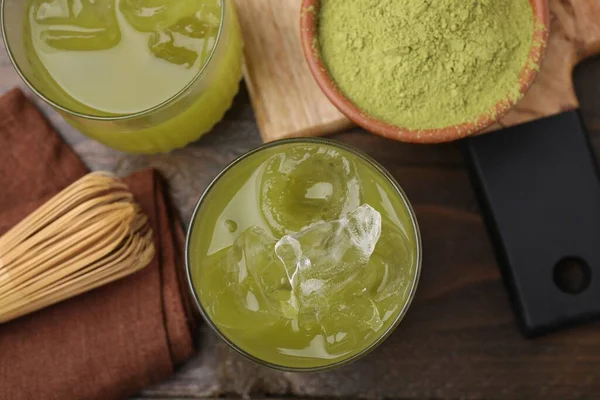 Delicious iced green matcha tea, powder and bamboo whisk on wooden table, flat lay