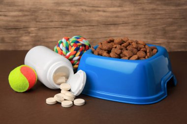 Kahverengi yüzeyde kuru hayvan mamasıyla, vitamin ve oyuncaklarla dolu bir kase.