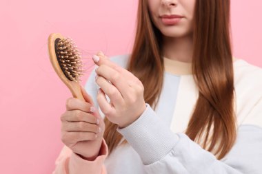 Pembe arka planda saçlarını fırçadan çözen kadın, yakın plan. Alopecia sorunu