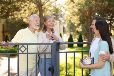 Friendly relationship with neighbours. Young family talking to elderly couple near fence outdoors clipart