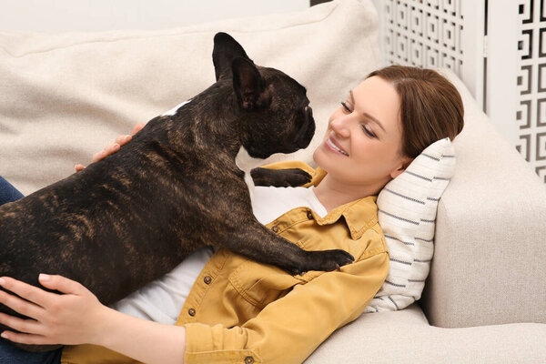 Happy woman with cute French Bulldog on soft sofa in room