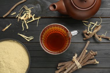 Fincanda Aromatik meyan kökü çayı, çaydanlık, kurutulmuş meyan kökü çubukları ve siyah ahşap masa üzerinde toz, düz uzanmış