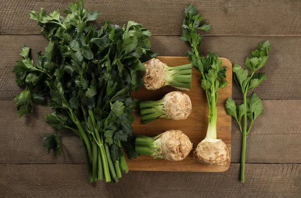 Fresh raw celery roots and stalks with leaves on wooden table, flat lay