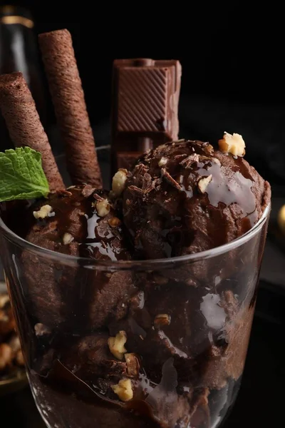 Tasty chocolate ice cream with sauce, nuts and wafer rolls in glass dessert bowl on table, closeup