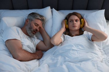 Evde yatakta horlayan kocasının yanında kulaklıkları olan sinirli bir kadın.