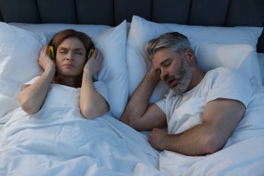 Evde yatakta horlayan kocasının yanında kulaklıkları olan sinirli bir kadın.