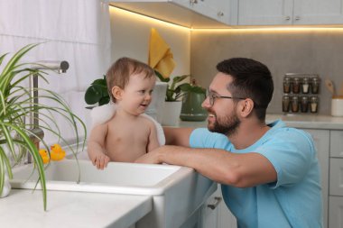 Babası küçük bebeğini evde lavaboda yıkıyor.