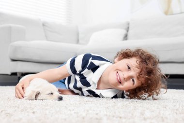 Bej halıda şirin köpek yavrusu olan küçük bir çocuk.