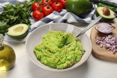 Lezzetli guacamole kasede ve malzemeler beyaz ahşap masada, yakın plan.