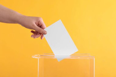 Oy sandığına oy veren kadın turuncu arka planda, yakın plan.