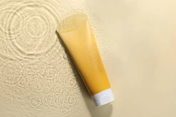 Tube of face cleansing product in water against beige background, top view