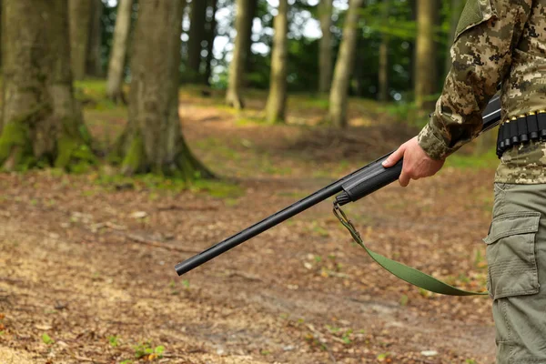 Man with hunting rifle wearing camouflage in forest, closeup. Space for text