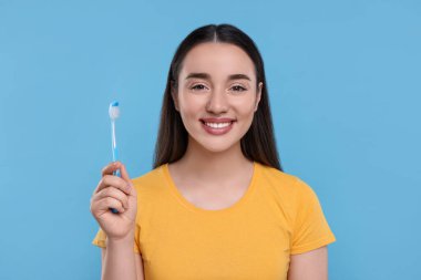 Açık mavi arka planda plastik diş fırçası tutan mutlu genç kadın.