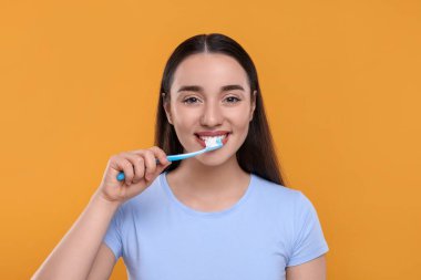 Mutlu genç bir kadın sarı arka planda plastik diş fırçasıyla dişlerini fırçalıyor.
