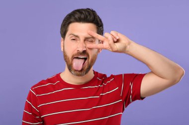 Dilini gösteren ve menekşe arkaplanda V işareti olan adam.