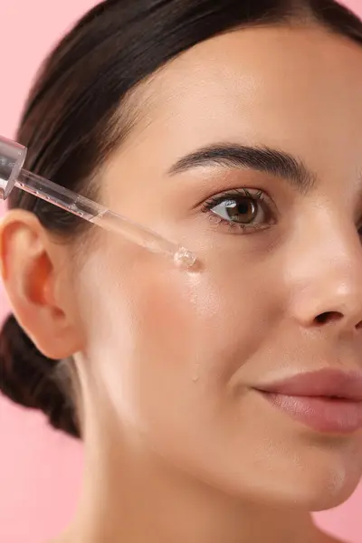 Beautiful Young Woman Applying Serum Her Face Pink Background Closeup — Stock Photo, Image