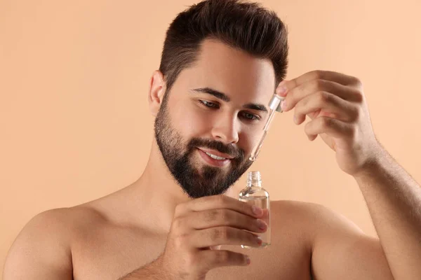 Handsome man with cosmetic serum in hands on beige background