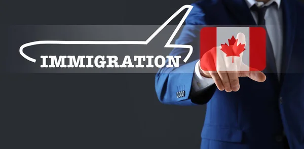 stock image Immigration. Businessman touching digital screen with illustration of airplane, word and flag of Canada on dark grey background, closeup