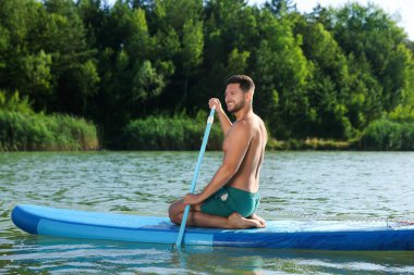 Nehirdeki SUP tahtasına kürek çeken adam.