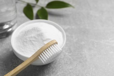 Bambu diş fırçası, yeşil yaprak ve gri masada bir kase kabartma tozu, yakın plan. Metin için boşluk