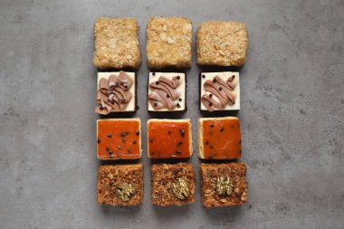 Farklı lezzetli pastaların parçaları gri masada, düz yerde.