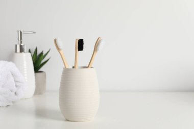 Bambu diş fırçaları kabın içinde, saksı bitkisi, havlu ve kozmetik ürünler beyaz tezgahın üzerinde, metin için boşluk