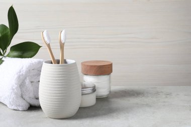 Bambu diş fırçaları tutacakta, havluda, pamuk pedlerde ve kremde açık gri masada, metin için boşluk
