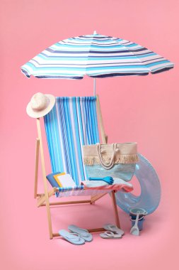 Güverte sandalyesi, şemsiye ve pembe arka planda diğer plaj aksesuarları. Yaz tatili