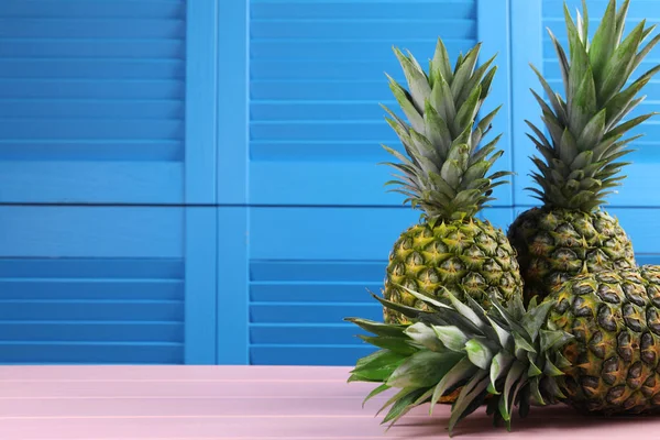 Delicious ripe pineapples on pink table near blue wall. Space for text