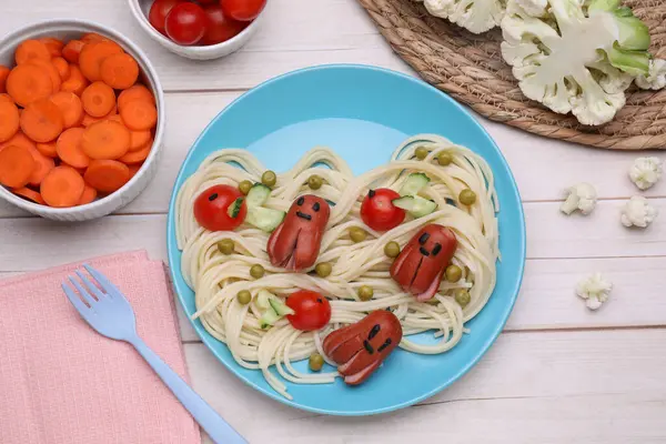 Creative serving for kids. Plate with cute octopuses made of sausages, pasta and vegetables on white wooden table, flat lay