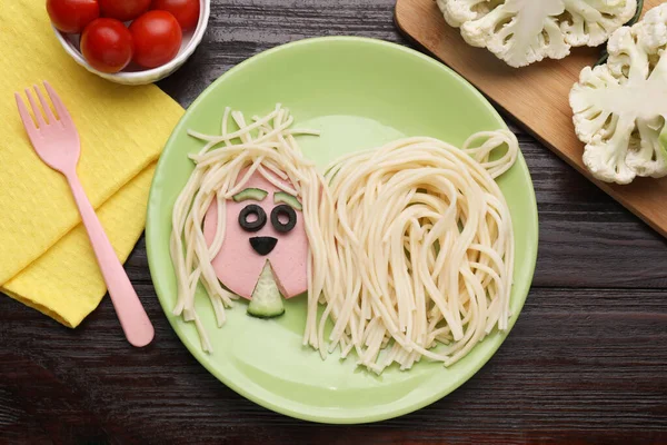 Creative serving for kids. Plate with cute dog made of tasty pasta, sausage and cucumber on wooden table, flat lay