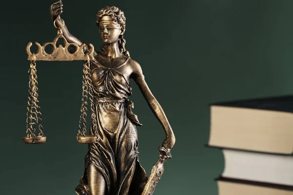 Statue of Lady Justice near books on green background, closeup and space for text. Symbol of fair treatment under law