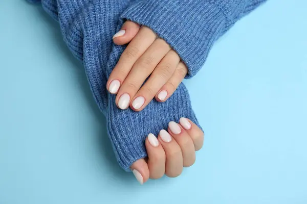 Woman showing her manicured hands with white nail polish on light blue background, top view