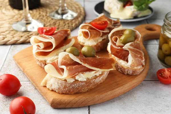 Tasty sandwiches with cured ham, tomatoes and olives on tiled table, closeup