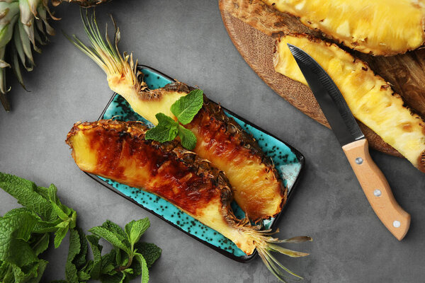 Tasty grilled and fresh pineapple pieces on grey textured table, flat lay