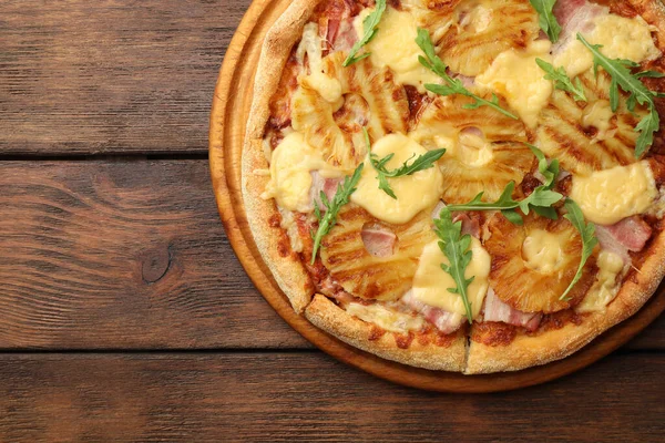 Delicious pineapple pizza with arugula on wooden table, top view. Space for text