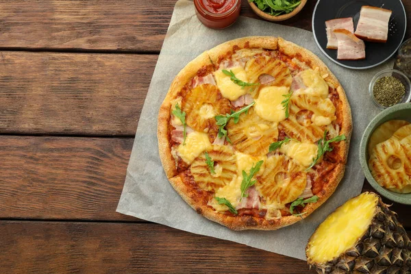 Delicious pineapple pizza and ingredients on wooden table, flat lay. Space for text