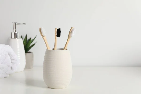 Bamboo toothbrushes in holder, potted plant, towel and cosmetic product on white countertop, space for text
