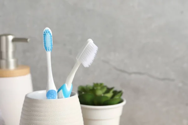 Plastic toothbrushes in holder on grey background, closeup. Space for text