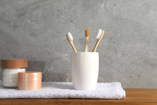 Bamboo toothbrushes in holder, towel and cosmetic products on wooden table