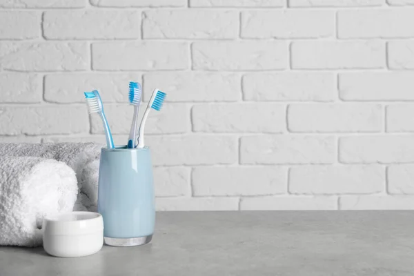 Plastic toothbrushes in holder, cosmetic product and towels on light grey table. Space for text