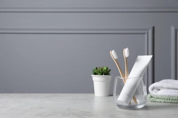 Bamboo toothbrushes in holder, toothpaste, houseplant and towels on light grey table. Space for text
