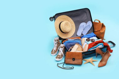 İçinde giysiler, plaj aksesuarları ve açık mavi arka planda ayakkabılar olan bavulu aç, mesaj için yer aç. Yaz tatili