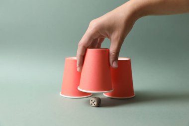 Soluk zeytinli arka planda bardağın altındaki zarları gösteren kadın, yakın plan. Thimblerig oyunu