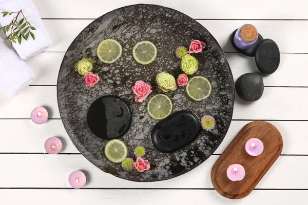 Plate with water, flowers, lime slices and burning candles on white wooden floor, flat lay. Pedicure procedure