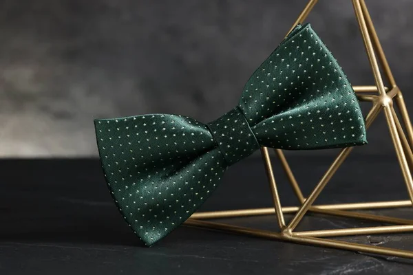 Stylish presentation of green bow tie on black table against gray background