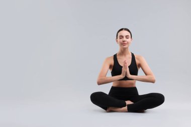 Gri arka planda yoga yapan güzel bir genç kadın. Mesaj için yer var. Lotus pozu