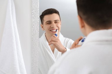 Adam banyoda aynanın yanında dişlerini elektrikli diş fırçasıyla fırçalıyor.