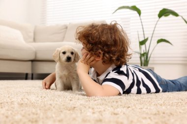 Bej halıda şirin köpek yavrusu olan küçük bir çocuk.