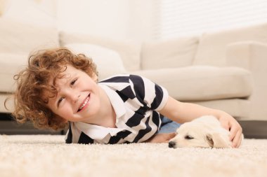 Bej halıda şirin köpek yavrusu olan küçük bir çocuk.